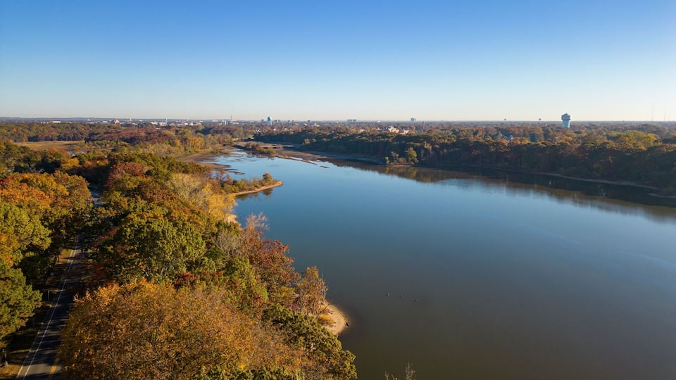 A river winding through a forested area with autumn foliage, a road parallel to the river, and distant cityscape.
