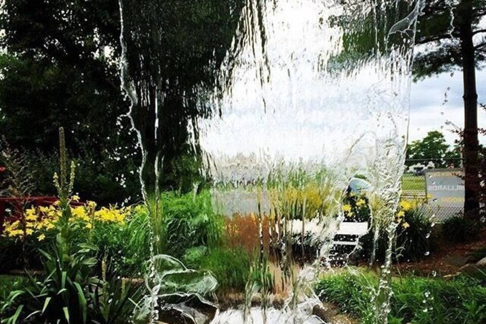 Una cascada fluye sobre rocas en un jardín con diversas plantas y flores.