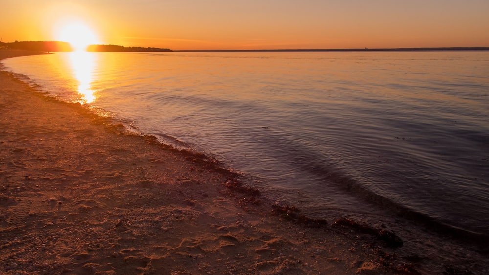 A sunset over a beach with calm waters and a distant shoreline.