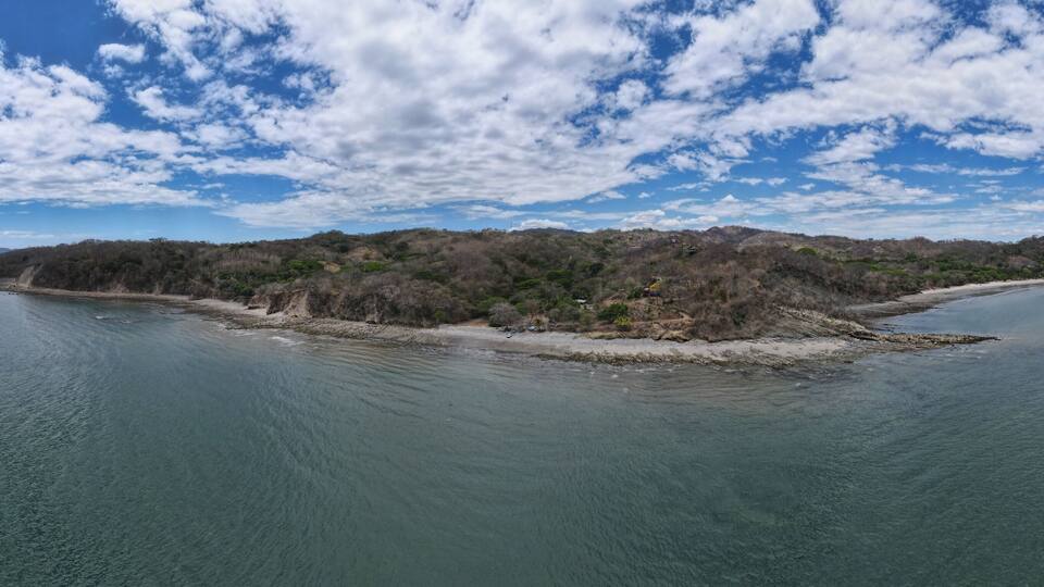 An aerial view of a small island with dense vegetation and a clear blue sky with scattered clouds.