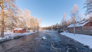 A river flowing through a snowy landscape with stone buildings and leafless trees.