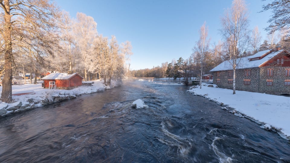 A river flowing through a snowy landscape with stone buildings and leafless trees.