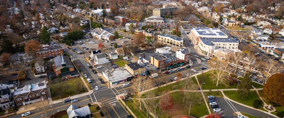 An aerial view of a town with a mix of residential and commercial buildings, a large dome structure, and a parking lot with cars.