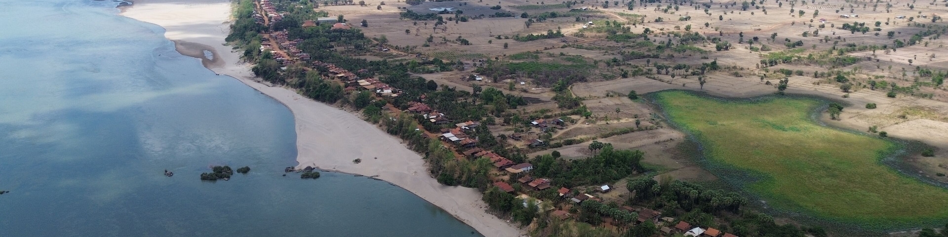 Vista aérea de un pueblo costero con playa, casas y campos de cultivo.