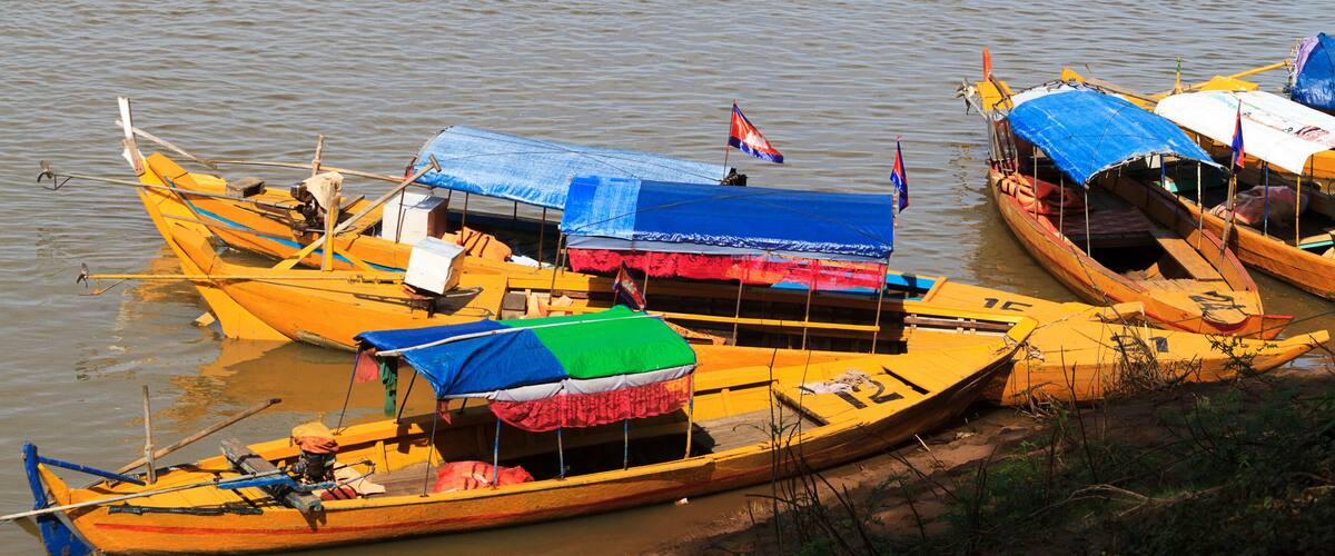 Several yellow boats with colorful canopies and flags, docked along a riverbank.