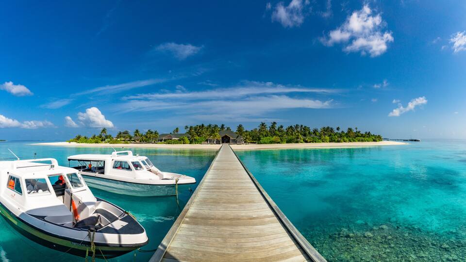 A wooden pier leading to a turquoise lagoon with two boats docked at the end.