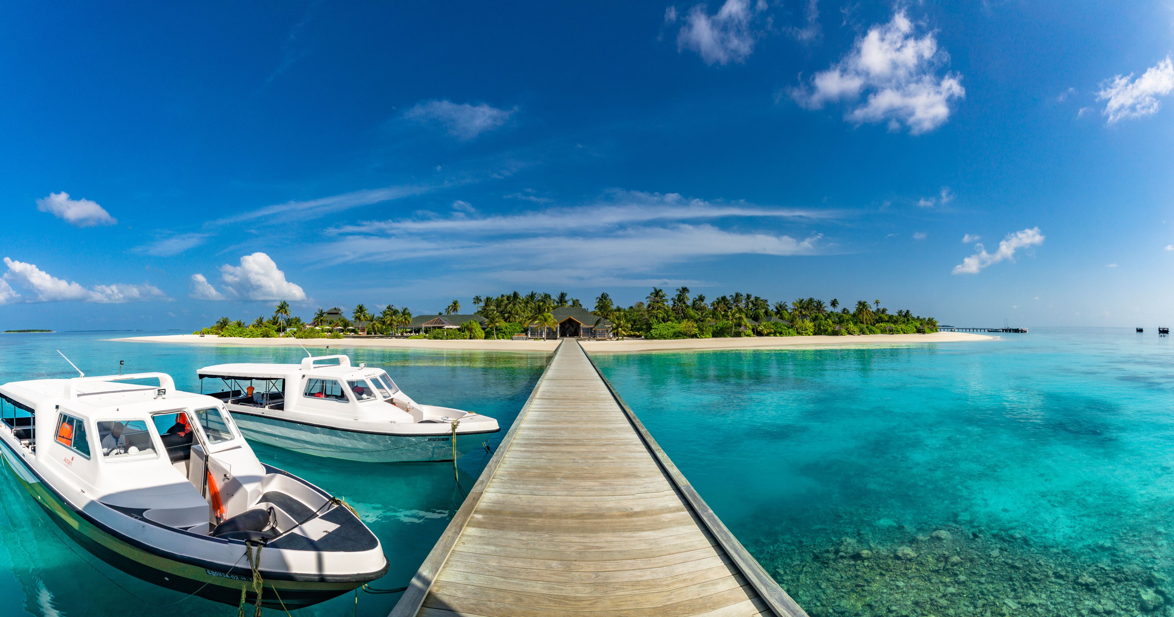 A wooden pier leading to a turquoise lagoon with two boats docked at the end.