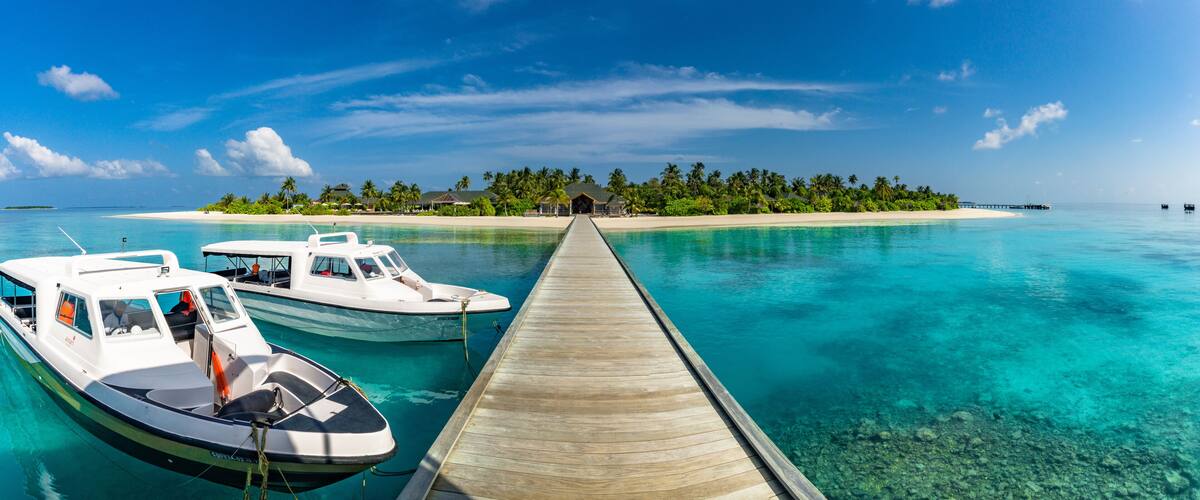 A wooden pier leading to a turquoise lagoon with two boats docked at the end.