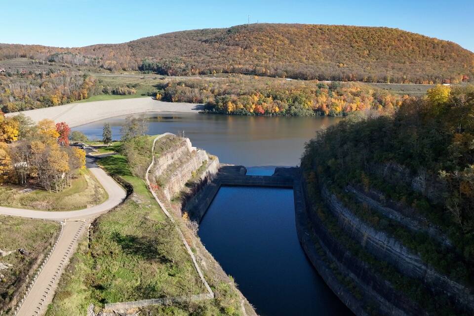 Una presa con un embalse, rodeada de follaje otoñal y colinas.