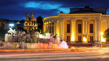 A night scene with a grand building and a fountain with statues.