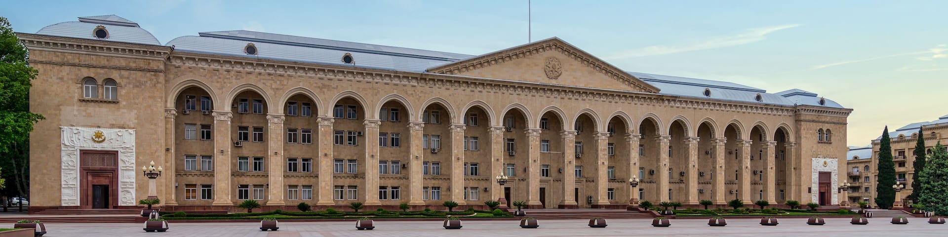 Ganja City Hall in Azerbaijan, a large beige building with an arched facade. It has many windows and a central entrance. A big plaza lies in front of it