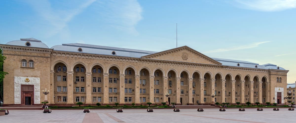A large, historic building with arched windows and columns, surrounded by a spacious plaza with planters.
