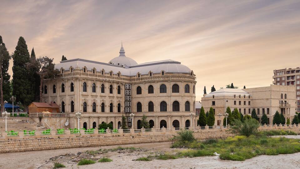 A historic building with a dome and arched windows, surrounded by trees and a river.