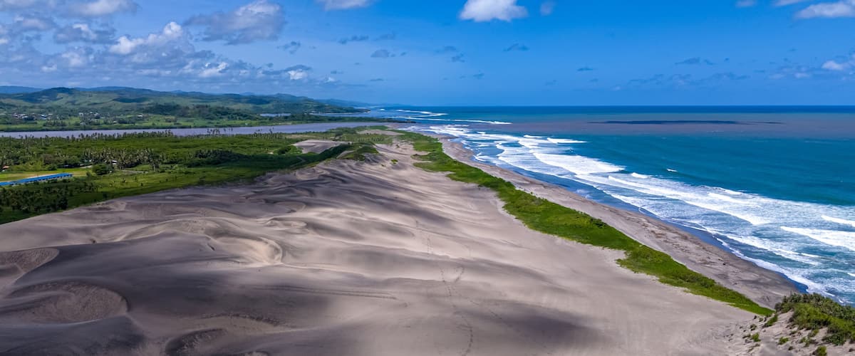 A coastal landscape with a sandy beach, ocean waves, and distant hills.