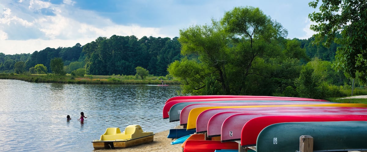 A view of the beach area at Lake Crabtree with people playing in the water with colorful canoe racks nearby in Morrisville, North Carolina.