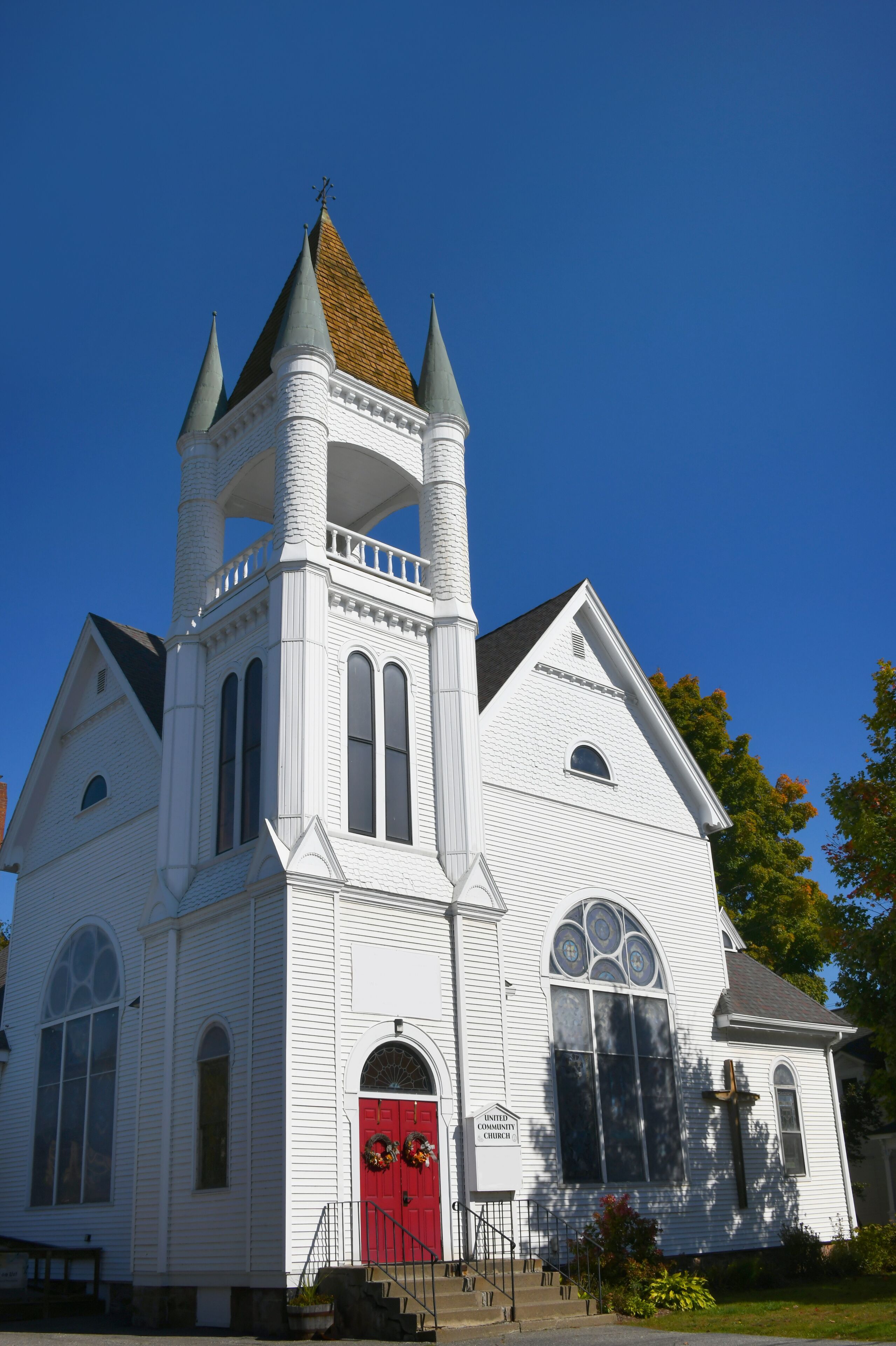 A white church with a red door, a bell tower, and a steeple.