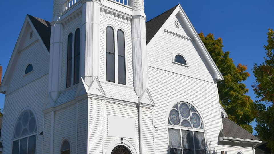 A white church with a red door, a bell tower, and a steeple.