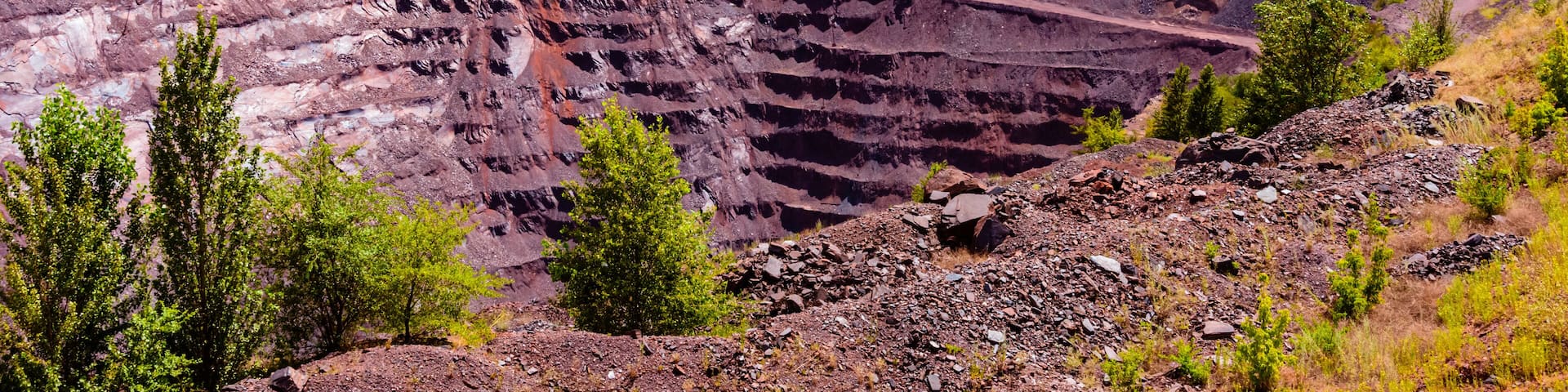 A large open-pit mine with layered earth and sparse vegetation.