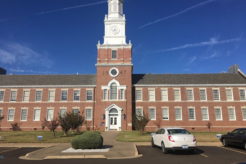 A large brick building with a clock tower and a white car parked in front.
