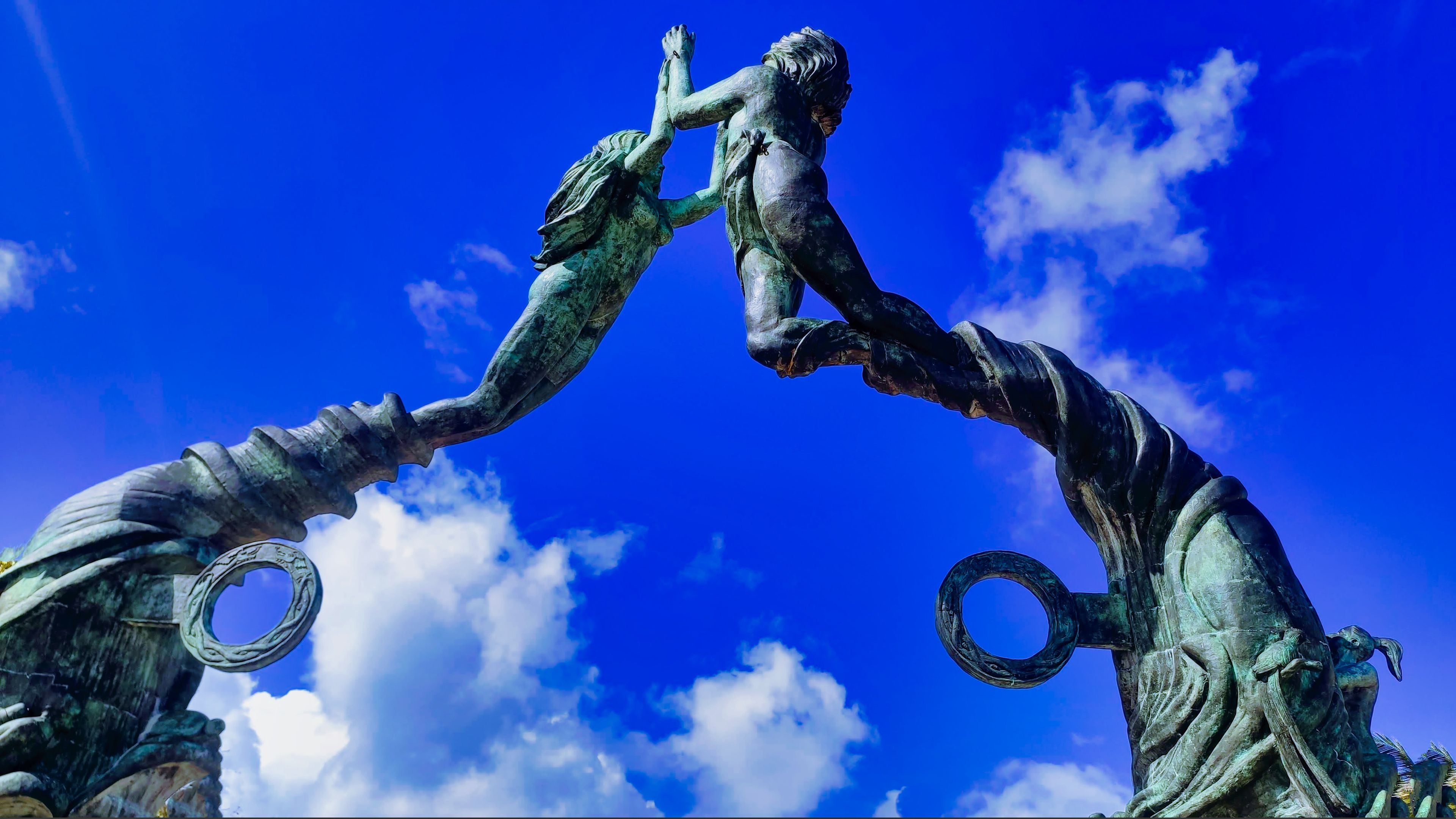 A bronze sculpture of a man and a woman reaching out to each other against a blue sky.