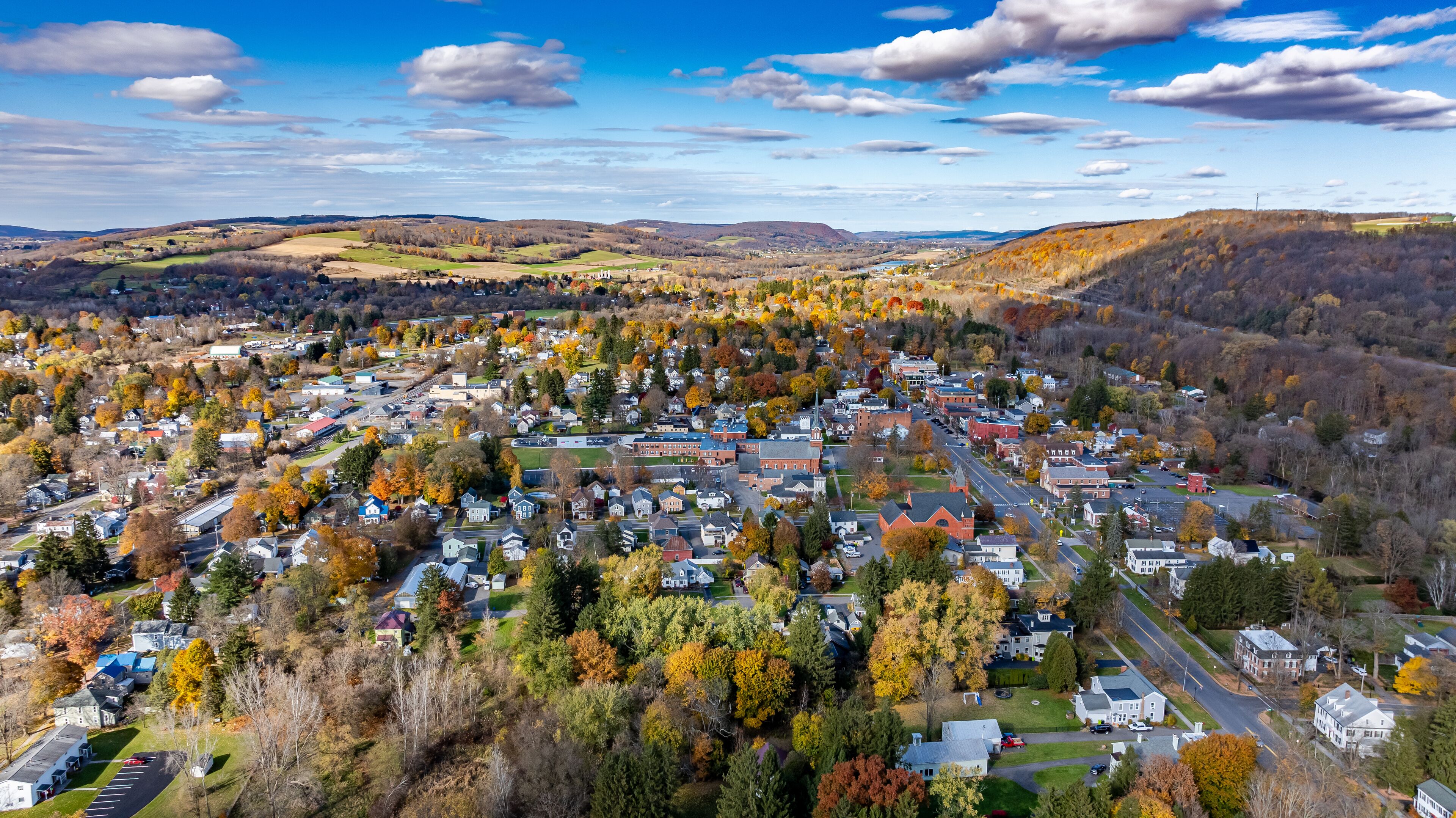 A town surrounded by autumn-colored trees and rolling hills.