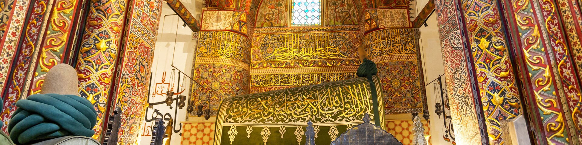 Un interior ornamentado con diseños intrincados, un reloj y un letrero que dice 'HAZRET MEVLANA'.