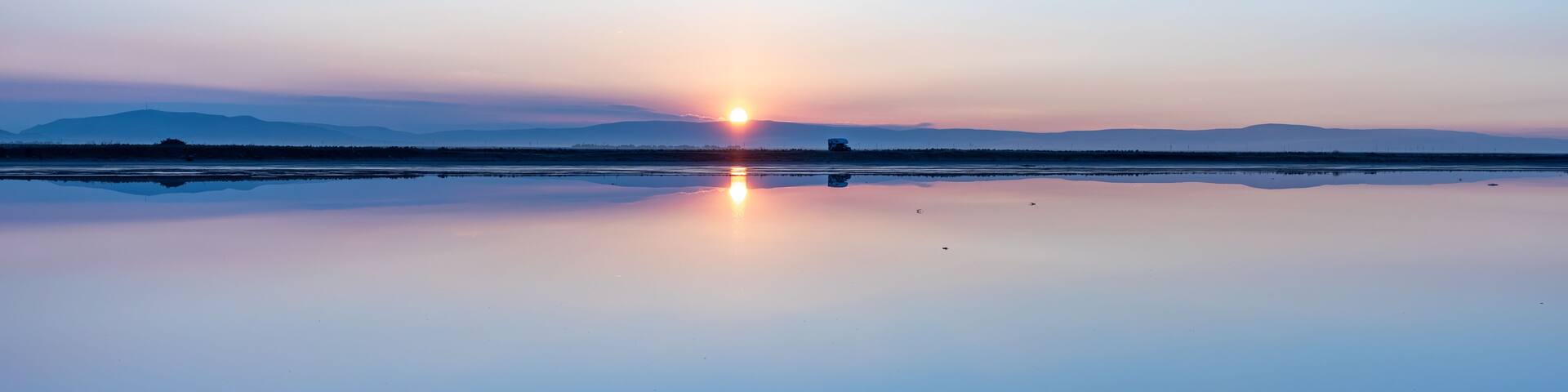 A calm lake reflecting the sunset with mountains in the distance.