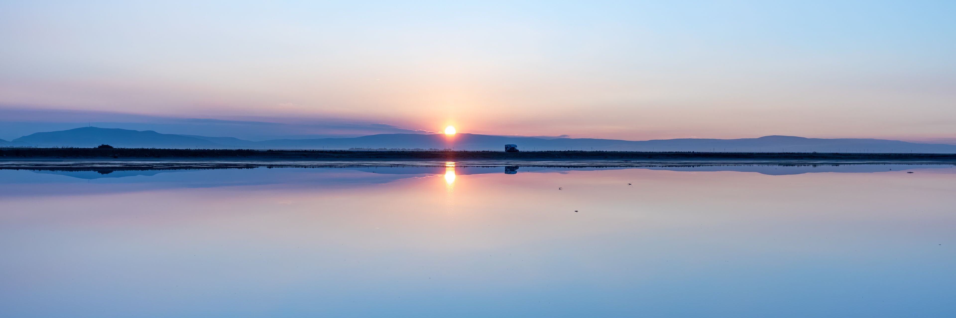 A calm lake reflecting the sunset with mountains in the distance.