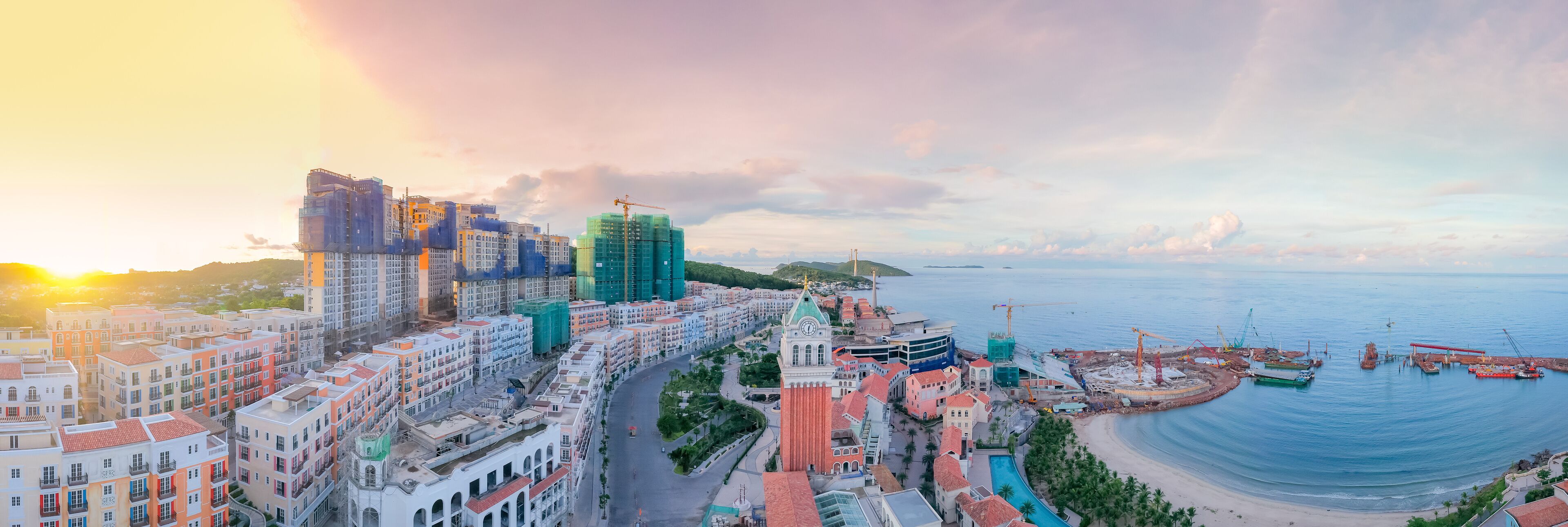A coastal cityscape with colorful buildings, a marina, and a sunset.