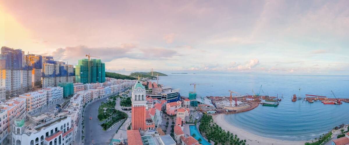 A coastal cityscape with colorful buildings, a marina, and a sunset.