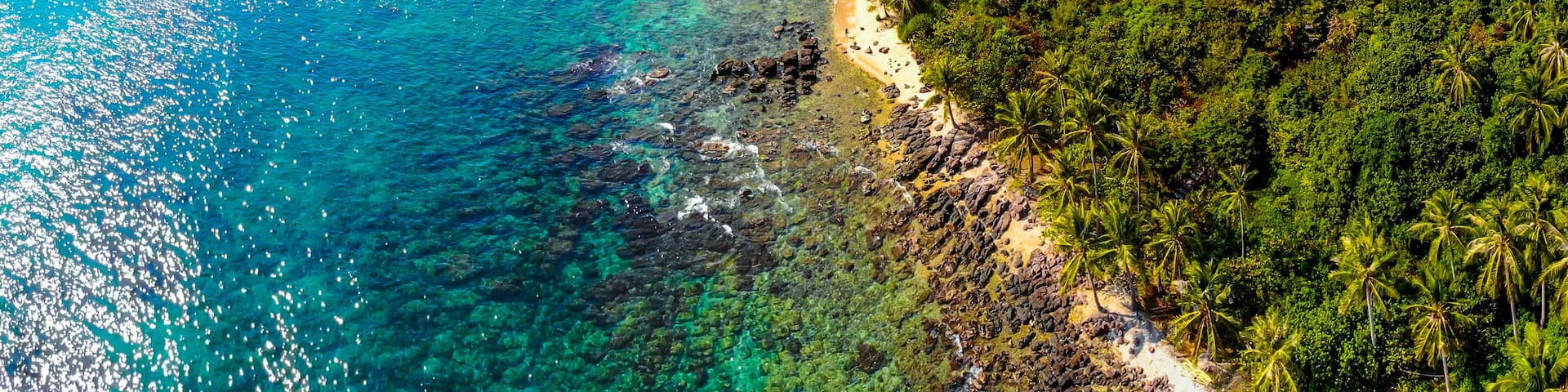 A coastal landscape with clear turquoise waters, a sandy beach, and dense tropical vegetation.