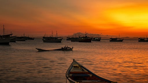 Um pôr do sol sobre um mar calmo, com vários barcos ancorados.