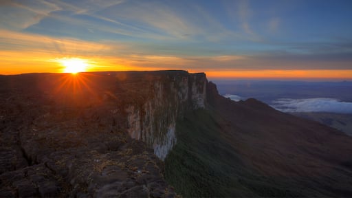 A mountain landscape with a sunrise or sunset, a clear sky, and a distant view of clouds.