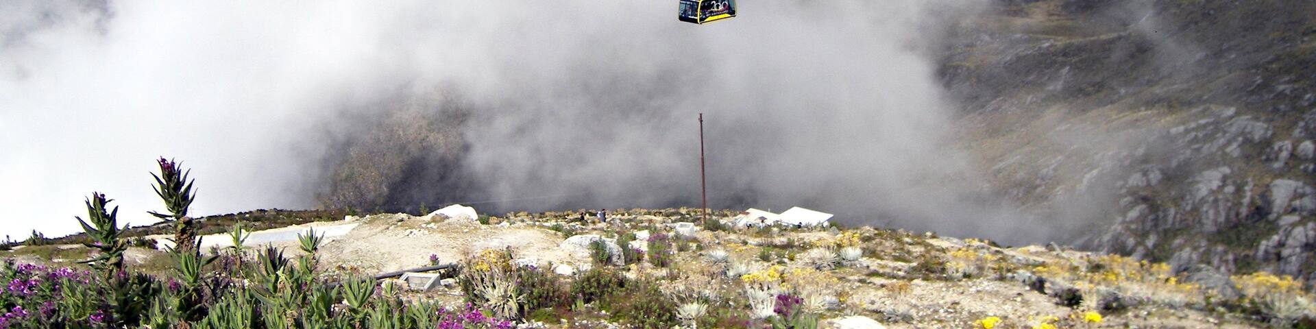 A cable car suspended over a mountainous landscape with sparse vegetation and rocky terrain.