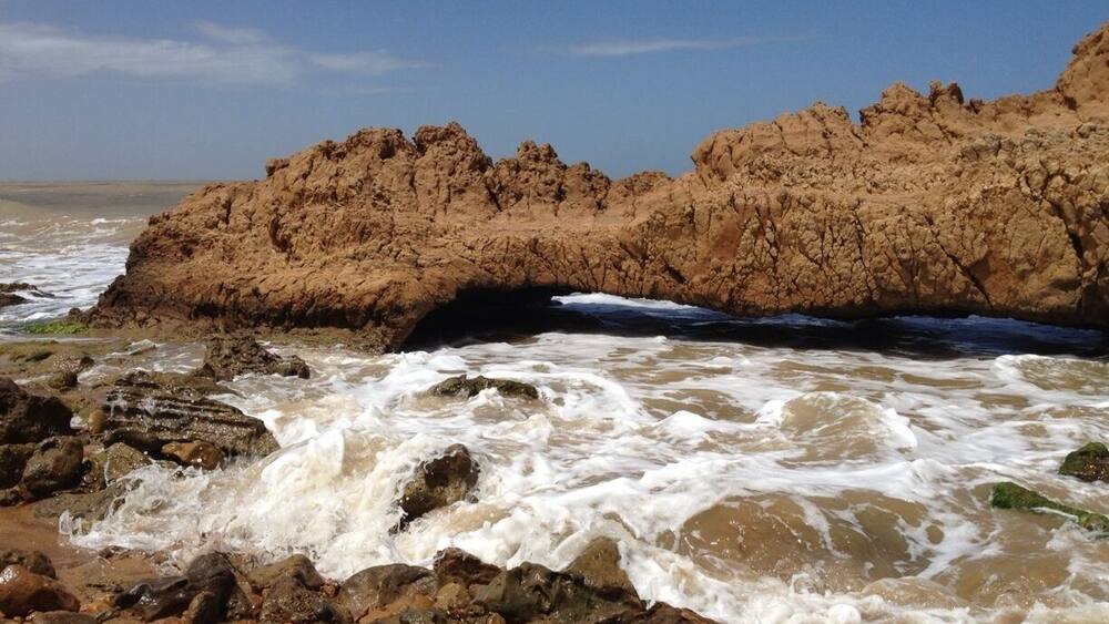 A rocky shoreline with waves crashing against the rocks and a large rock formation in the background.