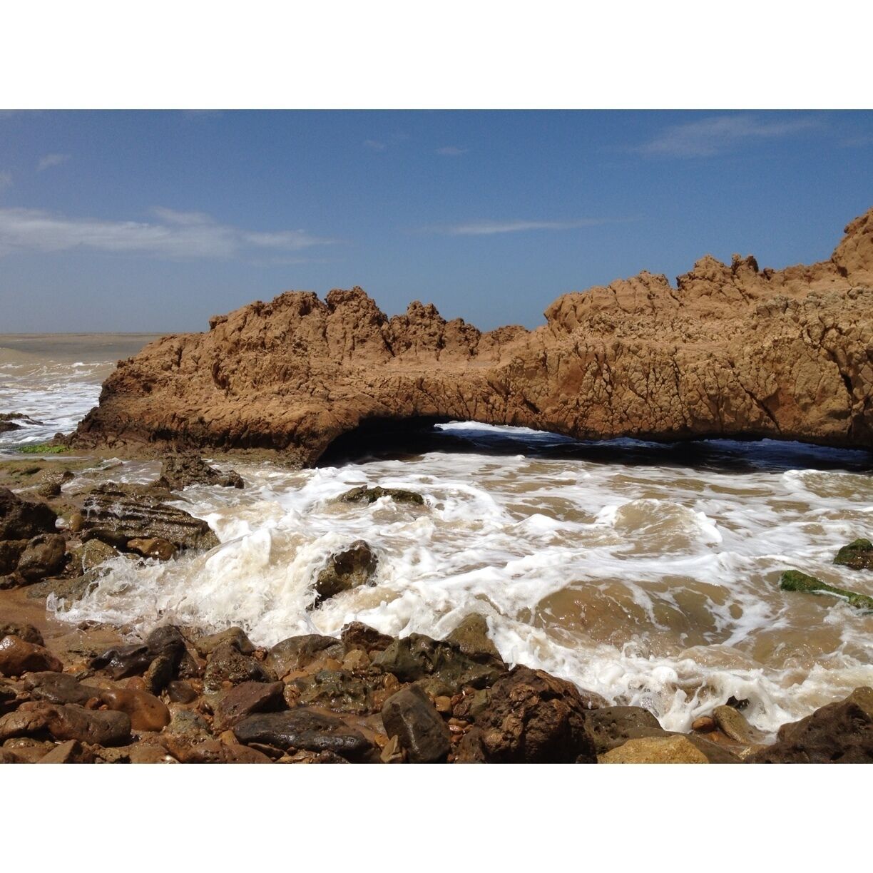 A rocky shoreline with waves crashing against the rocks and a large rock formation in the background.