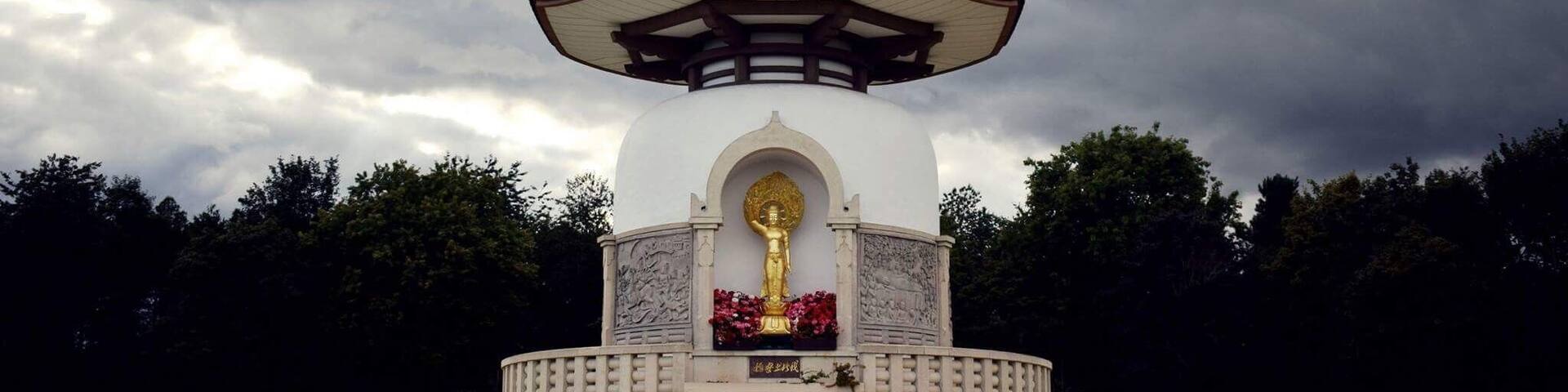 A pagoda-style structure with a golden statue on top, surrounded by a stone wall and a small staircase leading up to it.