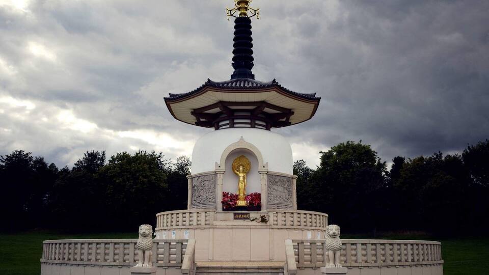 Edifici de tipus pagoda amb una estàtua daurada a la part superior, envoltat per una paret de pedra i una petita escala que hi mena.