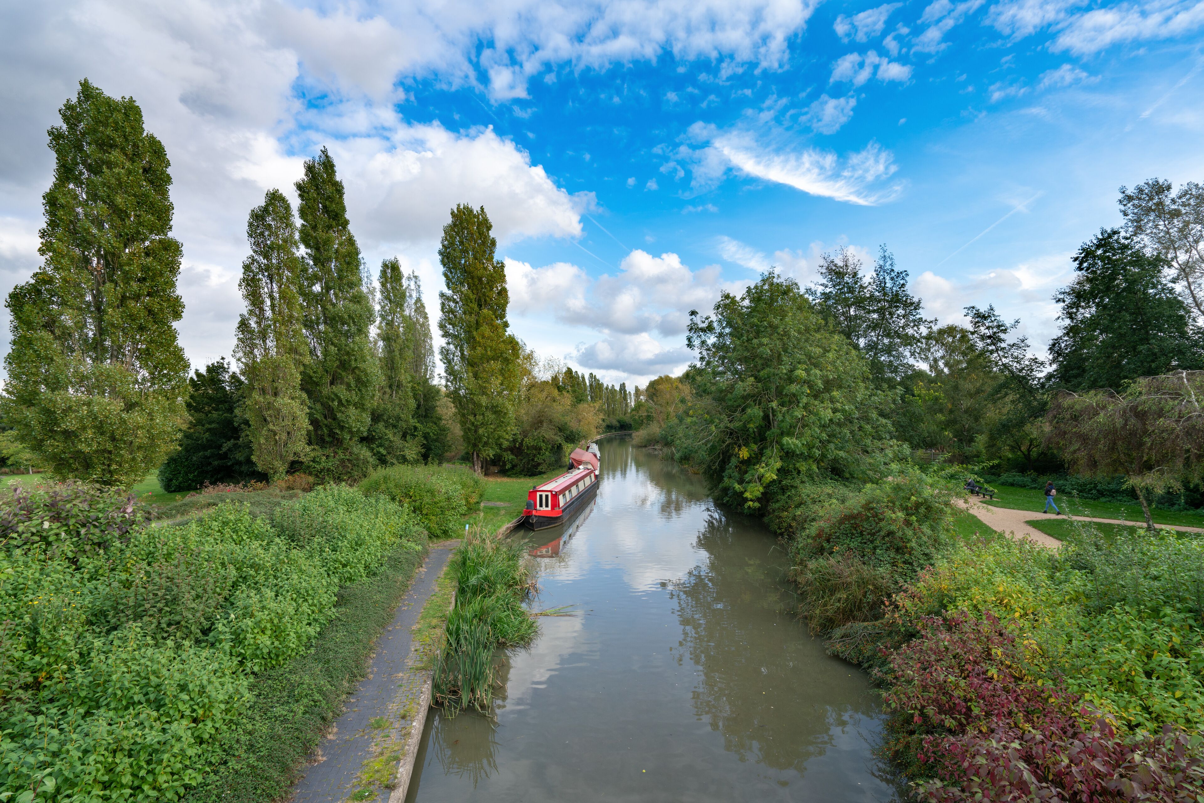 A narrow waterway with a red boat, surrounded by dense greenery and tall trees.
