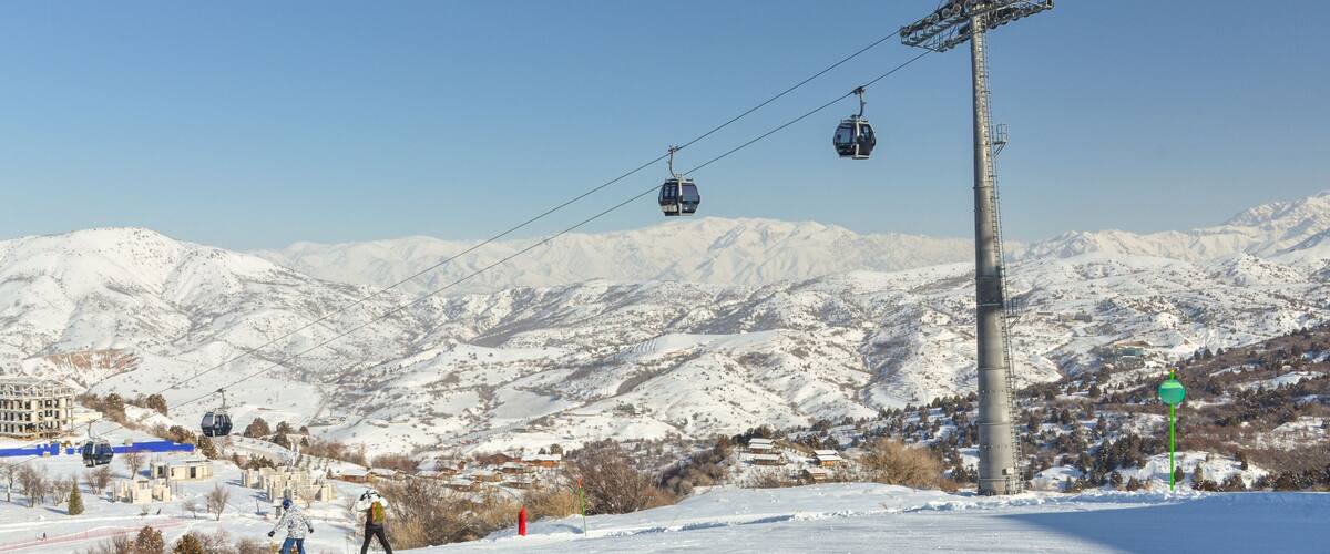 A snowy mountain landscape with a ski lift, buildings, and a clear sky.