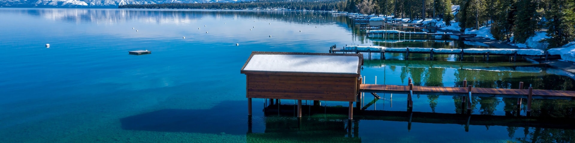 Pier, mountains with snow on calm Lake Tahoe, Homewood, California, United States of America.