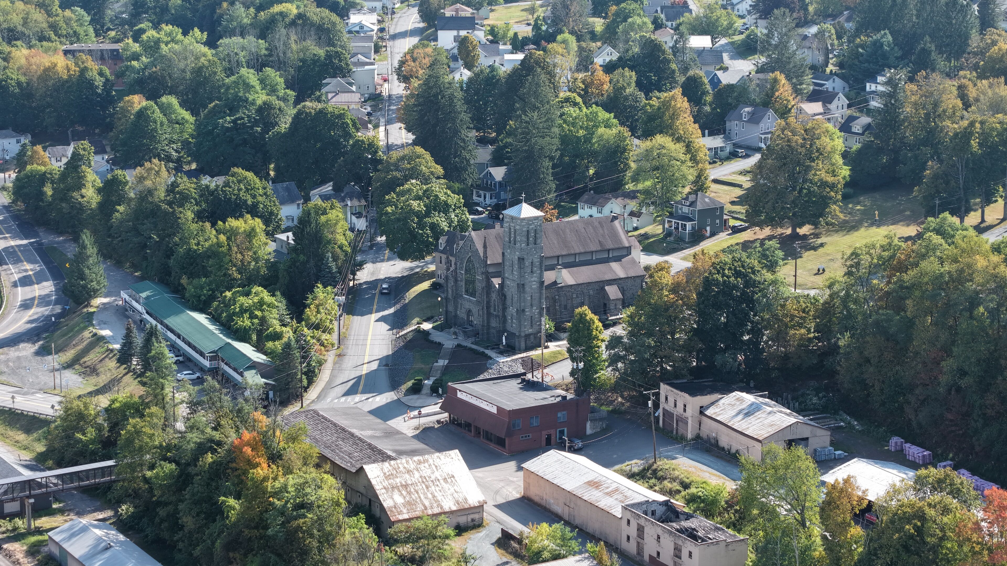 Aerial view of the historic gray stone church steeple piercing through the lush autumn foliage, a testament to time and faith, Honesdale, Pennsylvania, United States.
