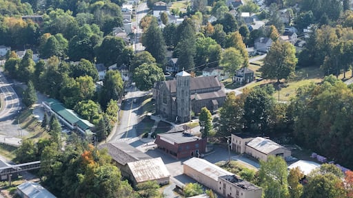 Aerial view of the historic gray stone church steeple piercing through the lush autumn foliage, a testament to time and faith, Honesdale, Pennsylvania, United States.