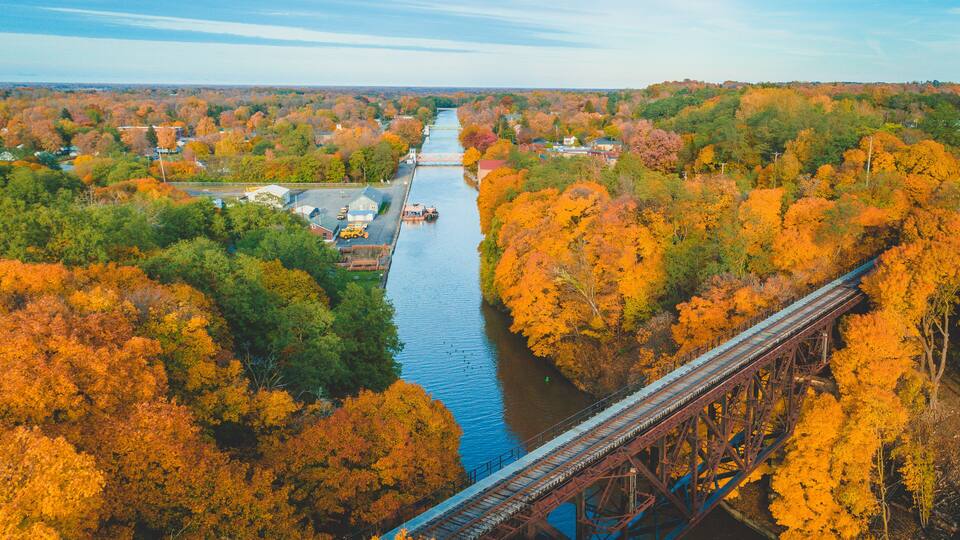 A river with a bridge, surrounded by autumn-colored trees.