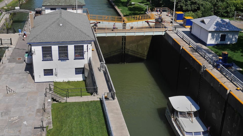 A lock system with a boat passing through, a bridge, and a river surrounded by greenery.