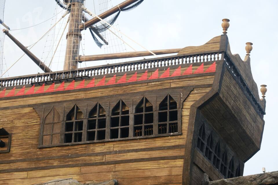 Proa de barco de madera con detalles rojos y una barandilla decorativa.