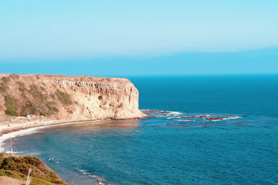 Una scogliera a picco sul mare con una spiaggia e affioramenti rocciosi.