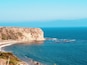 Una scogliera a picco sul mare con una spiaggia e affioramenti rocciosi.
