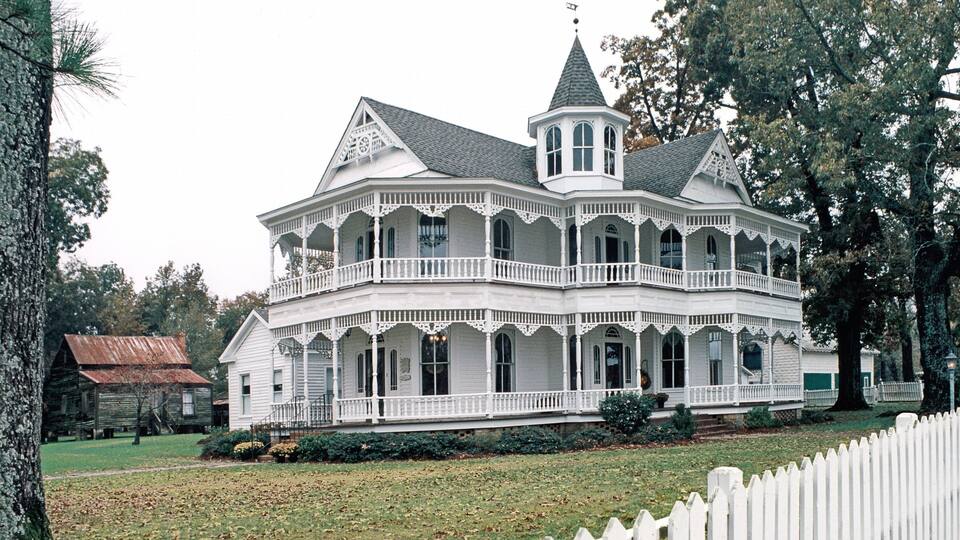 A large white Victorian-style house with a wrap-around porch and a tower.