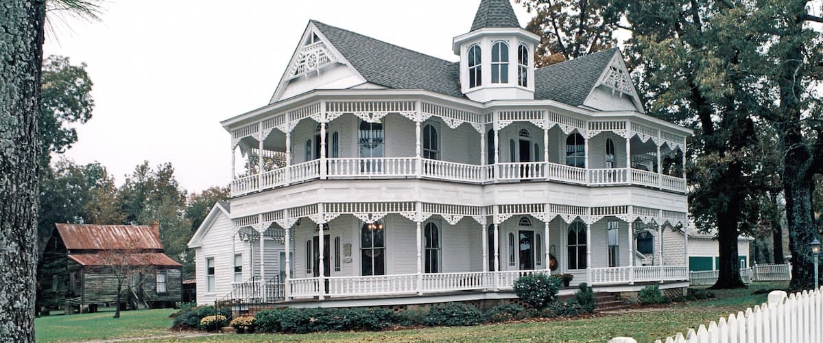 A large white Victorian-style house with a wrap-around porch and a tower.